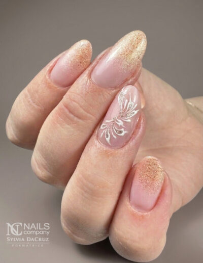 Pose d'ongles nude avec dégradé de paillettes dorées et arabesque blanche faite main par Sylvia Da Cruz à Sancé.